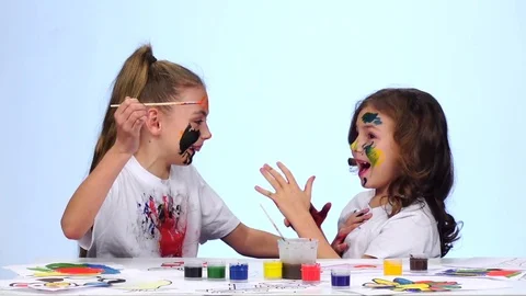 Kid sitting at the table applying paints to their clothes. White background Stock Footage 76131224