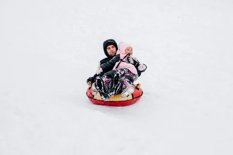 Kid smiling and sliding down hill on sled with father looking away wearing warm Stock Photos