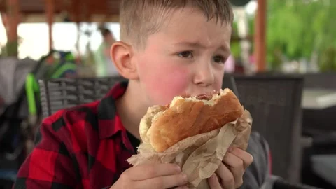 Kid snacks with burger while walking in the park Stock Footage 246978425