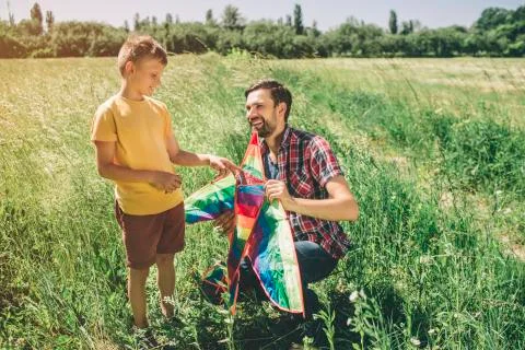 Kid is standing while his dad is sitting in squatt position. THey are holding Foto stock