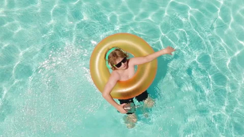 Kid stands inside orange inflatable swim ring. Kid wears headphones and dark Stock Footage 344077824