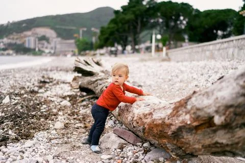 Kid stands near the old deck on the pebble beach, turning his head Stock Photos