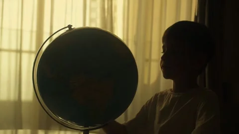 Kid studies a large globe in his bedroom against warm golden hour window light Stock Footage 344818420