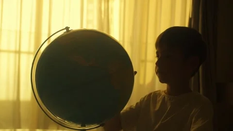 Kid studies a large globe in his bedroom against warm golden hour window light 스톡 동영상 348025551