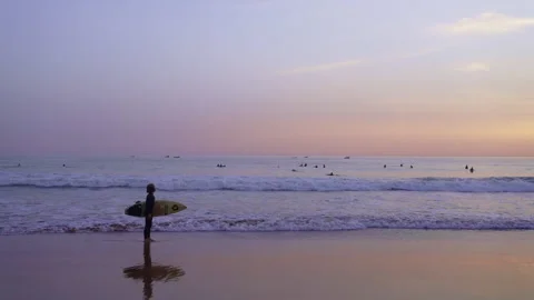 Kid surfer afraid of the sea walking on the shore at sun set holding a surfboard Stock Footage 296658561