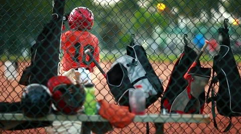 Kid swinging his baseball bat.  Bags and helmets seen from behind fence 動画素材 47712882