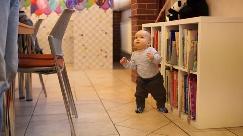 The kid takes his first steps at home near the bookcase. Kids development Stock Footage 103308025