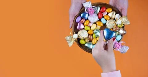 Kid taking hearth shape wrapped chocolate, top view holding bowl of candies. Stock Photos