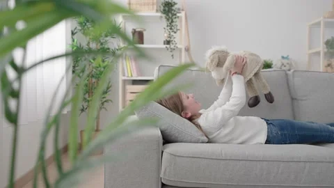 Kid talking to soft toy laying on sofa Stock Footage 235308992