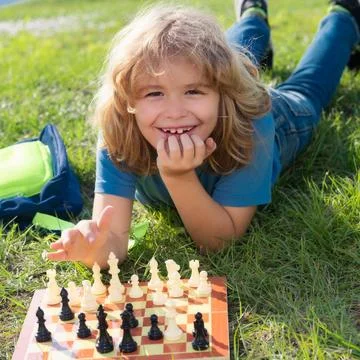 Kid thinking about chess laying on grass in summer park. The concept of learning Stockfoto's