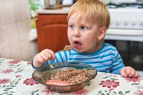 The kid is three years eats buckwheat with sausage Stock Photos