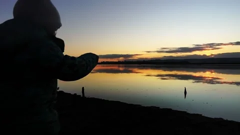 Kid throwing a stone into mirror looking sunset lake Stock Footage 171522343