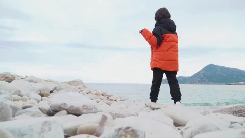 Kid throwing stones to the sea from the beach in winter Stock Footage 284077481