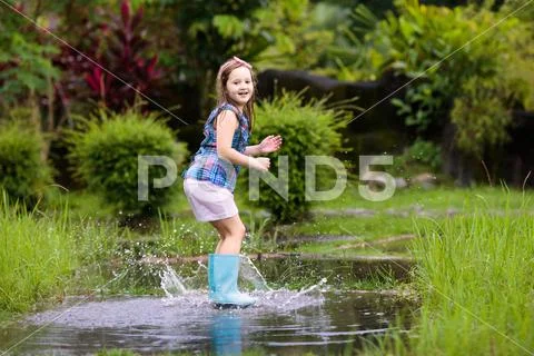 Kid with umbrella playing in summer rain. Stock Photos