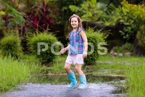 Kid with umbrella playing in summer rain. Stock Photos