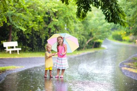 Kid with umbrella playing in summer rain. Stock Photos