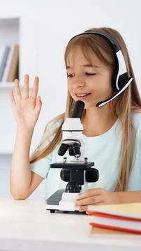 Kid uses a microscope and wears a headset while learning in a classroom Stockfoto's