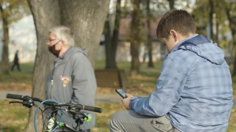 Kid using smartphone while man wearing protective mask and walking in park Stock Footage 143151462