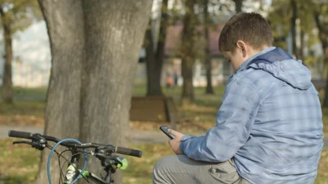 Kid using smartphone while sitting on bench in park Stock Footage 143149341