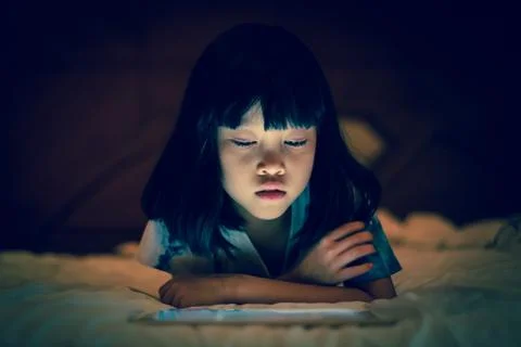 Kid using tablet in dark bedroom background. Stock Photos