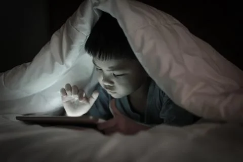 Kid using tablet while lying under blanket. Stock Photos