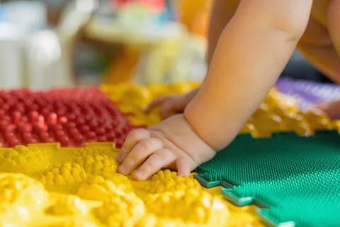 The kid walks barefoot on multi-colored massage rugs. Stock Photos