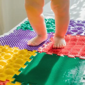 The kid walks barefoot on multi-colored massage rugs. Stock Photos