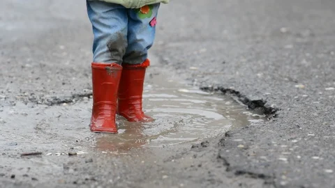 The kid walks through a puddle on the road in the rain in spring Stock Footage 129935606