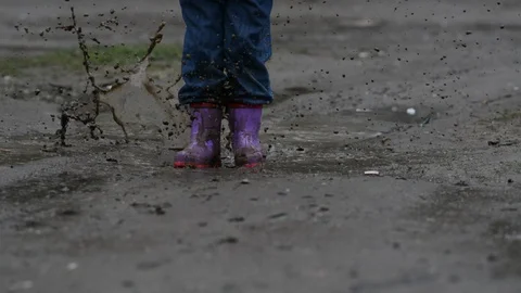 Kid walks through a puddle on the road in the rain in spring. Stock Footage 129935771