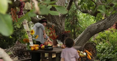 Kid watching how mother cut pumpkin under huge tree outdoors Stock Footage 165289470