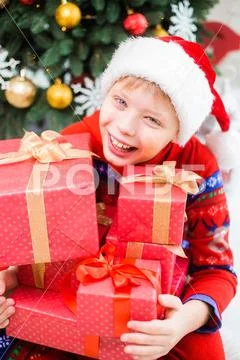 Kid wearing red santa hat and holding many present boxes in hands Stock Photos