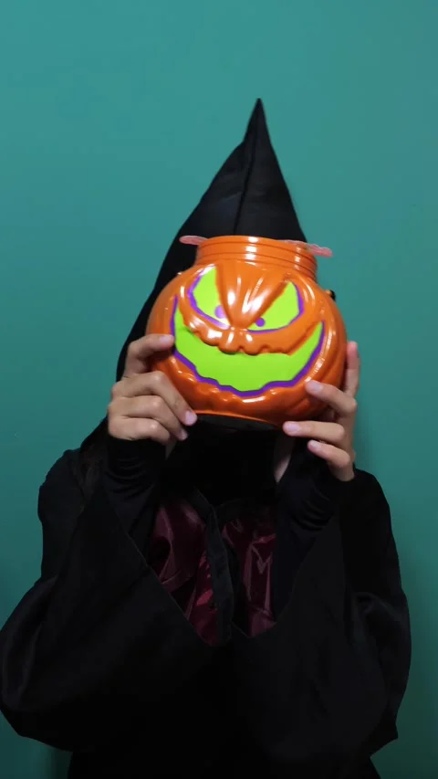 Kid in witch costume hides behind a grinning jack-o-lantern candy pail Stock Footage 343568574