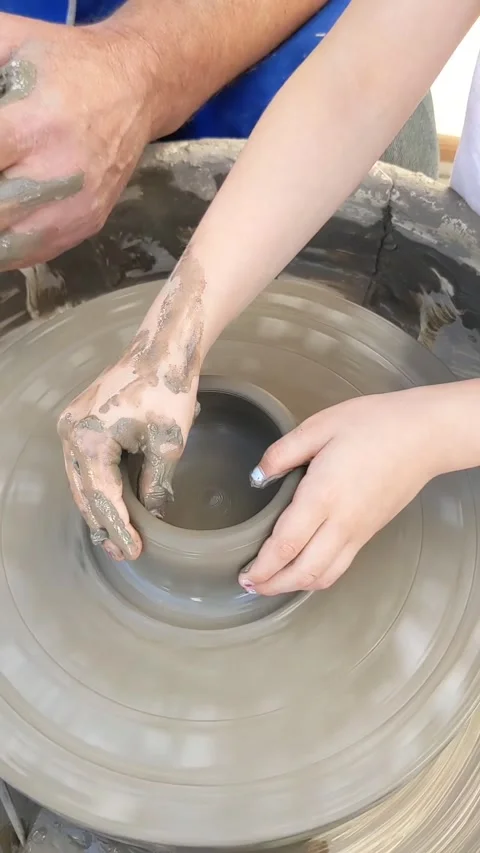 Kid working on potters wheel and making vase guided by a skilled ceramist. View Stock Footage 217340041