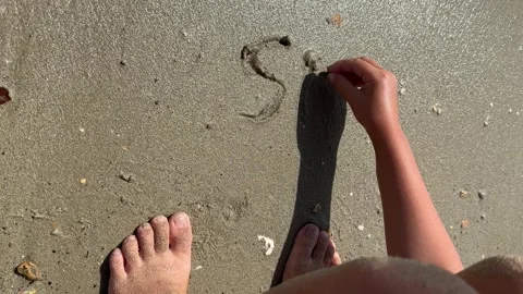 Kid writing by hand phrase SPF and drawing heart in sand by sea Stock Footage 246504047