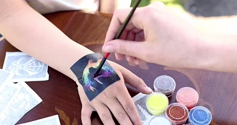 Kid's animator is creating sparkling glitter tattoo on a child's hand Stock Footage 250020108