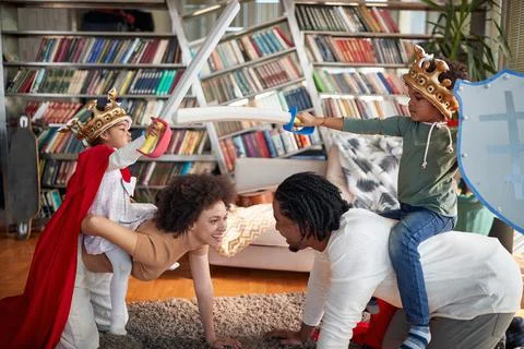 Kids are enjoying riding their parents while imitating knights at home. Famil Stock Photos