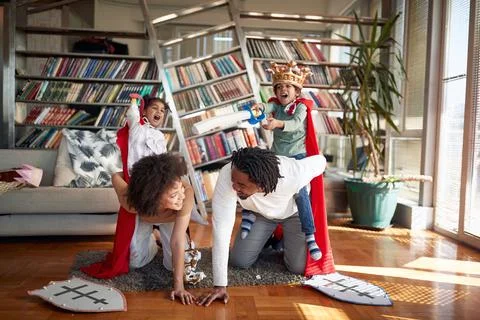 Kids are shouting while riding their parents in a knights game at home. Famil Stock Photos