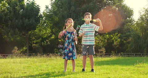Kids blowing soap bubbles, having fun outdoors on backyard on summer warm day Stock Footage 239855881