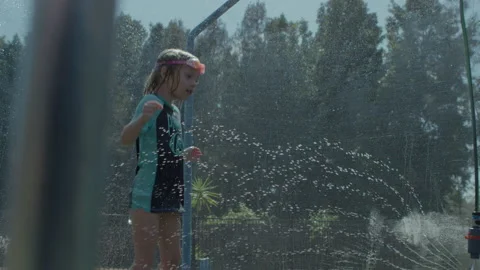 Kids bouncing on trampoline playing in summer with water Stock Footage 135789593