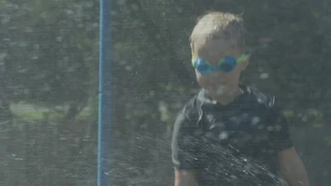 Kids bouncing on trampoline playing in summer with water mid shot Video stock 135789787