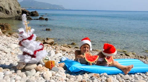 Kids in chrismas hat are eating watermelon on the beach Stock Footage