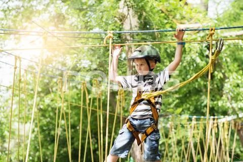 Kids climbing in adventure park. Boy enjoys climbing in the ropes course adve Stock Photos