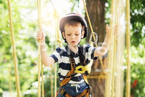 Kids climbing in adventure park. Boy enjoys climbing in the ropes course adve Stock Photos