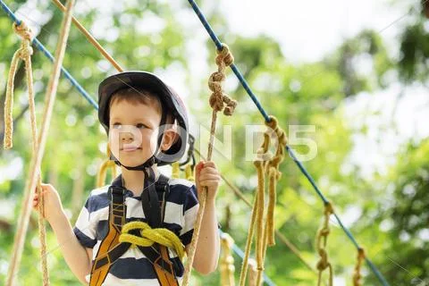 Kids climbing in adventure park. Boy enjoys climbing in the ropes course adve Stock Photos