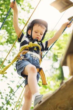 Kids climbing in adventure park. Boy enjoys climbing in the ropes course adve Stock Photos