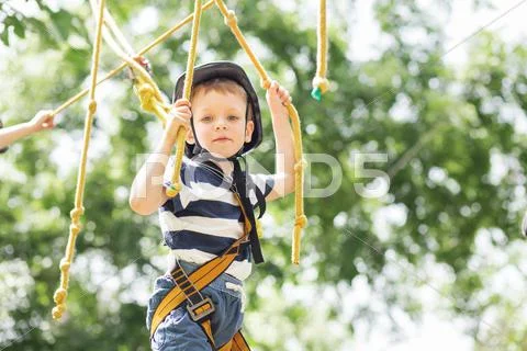 Kids climbing in adventure park. Boy enjoys climbing in the ropes course adve Stock Photos