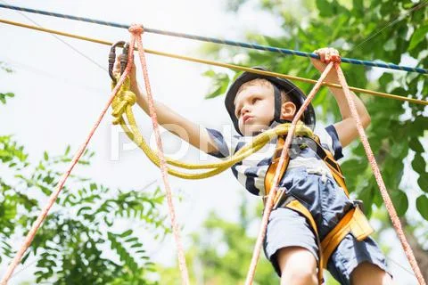 Kids climbing in adventure park. Boy enjoys climbing in the ropes course adve Stock Photos
