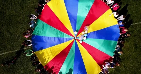 Kids collaborating in a old game using a parachute to bounce blow up beach Stock Footage 91926276