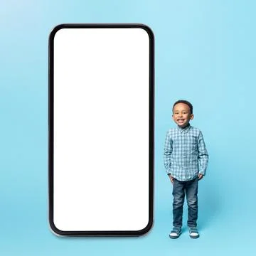 Kids content. Adorable little black boy standing near huge smartphone with blank Stock Photos