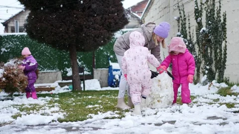 Kids creating a snowman in a cozy backyard on a winter afternoon Stock Footage 303509049